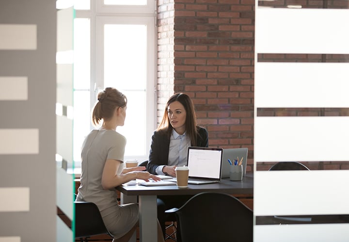 Dos mujeres conversan mientras trabajan con sus porttiles en una sala de reuniones